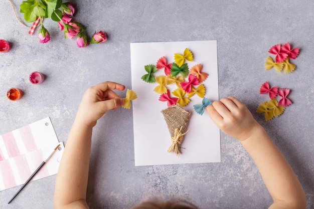 色紙と色パスタから花の花束をしている小さな子供 プレミアム写真