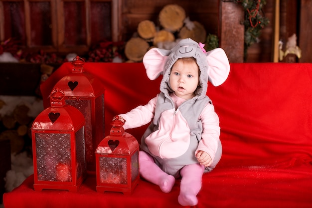 Small child (girl) in festive suit of mouse (rat) sits near flashlights and christmas decorations Premium Photo