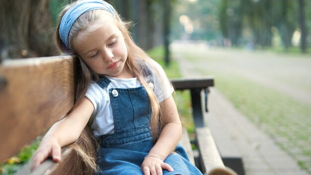 Premium Photo | Small tired child girl sitting on a bench with closed ...