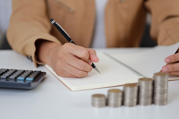 Premium Photo Smart And Active Asian Businesswoman Hands Writing Something On Notebook With Saving Growth On Stacking Coin On Table Meaning Of Earning Money Or Investment Or Tax For Business Advertising