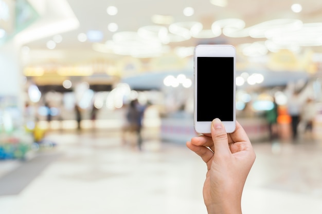 Smart phone with white screen in hand on blurred in shopping mall background,shopping online concept,shopping by smart phone... 