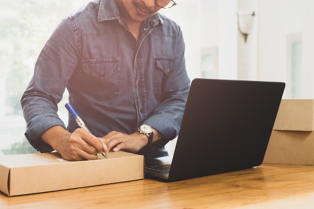 Sme business man writing address on parcel with labtop on the table. Premium Photo