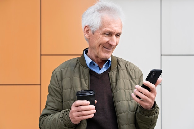 Smiley older man in the city using smartphone while having coffee Free Photo