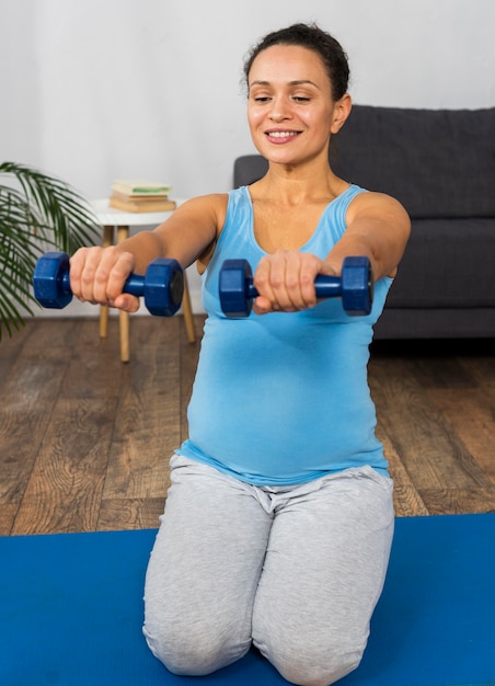 Premium Photo | Smiley pregnant woman training with weights at home on mat