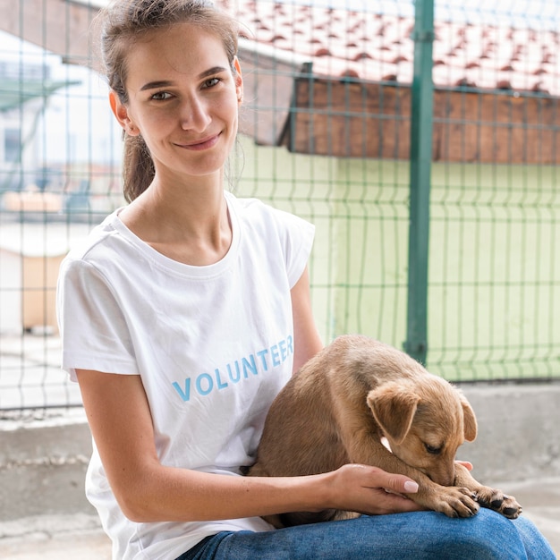 養子縁組のために犬を持ち上げる動物保護施設のスマイリー女性 無料の写真