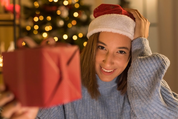 クリスマスプレゼントを保持しているサンタの帽子とスマイリーの女性 無料の写真