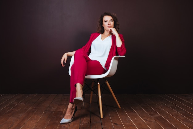 Smiley young businesswoman sitting on the office chair over dark background Free Photo