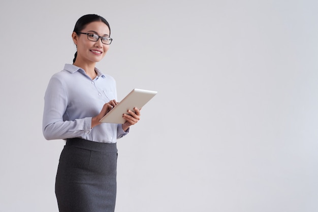 Smiling asian woman in glasses holding tablet computer and looking at camera Free Photo