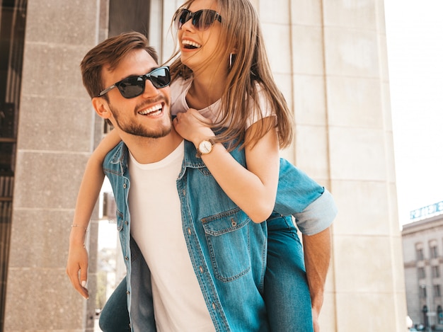 Smiling beautiful girl and her handsome boyfriend in casual summer clothes. man carrying his girlfriend on the back and she raising her hands. Free Photo
