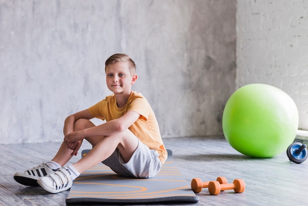 Smiling Boy Sitting On Exercise Mat With Dumbbell Pilates Ball