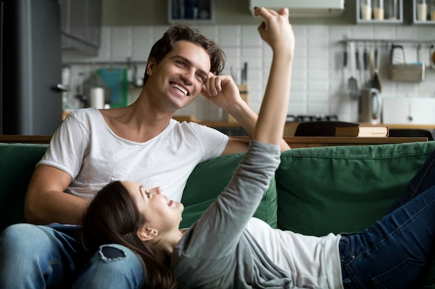 Smiling couple having fun with smartphone taking selfie at home Free Photo