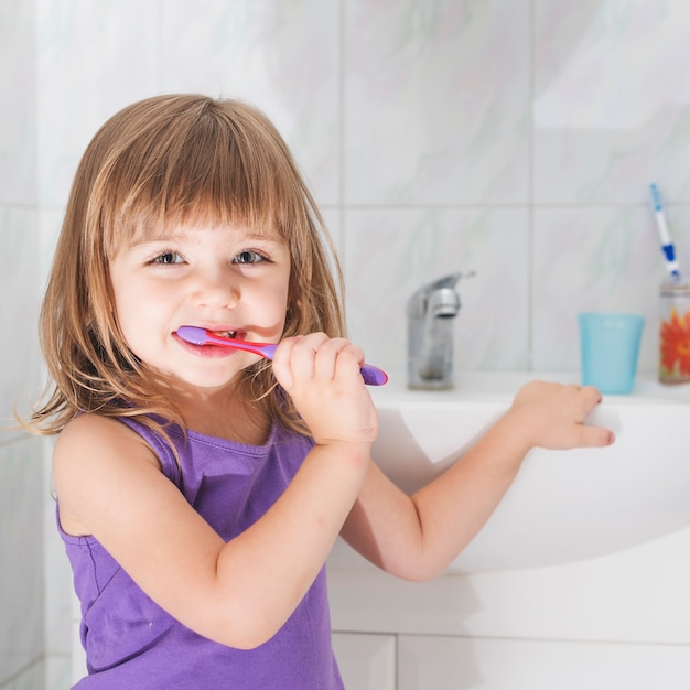 Smiling girl holding toothbrush standing in front of washroom sink