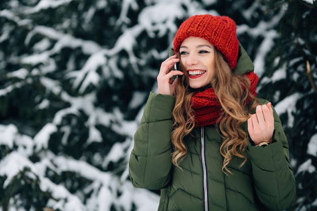  Smiling girl in red winter hat and scarf talking on smartphone  Free Photo