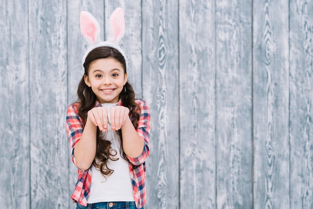 灰色の木製の机に対してウサギのようにポーズをとってウサギの耳を持つ少女の笑顔 無料の写真