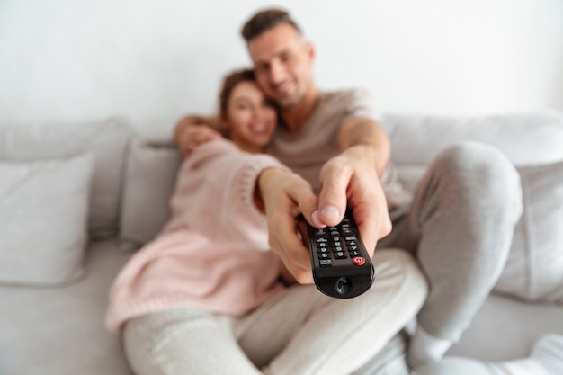 Smiling loving couple sitting on couch together and watching tv. focus on tv remote Free Photo