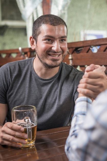 Smiling man arm wrestling with friend in bar Free Photo