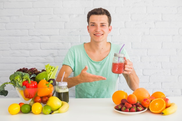 Smiling man holding red smoothie jar offering fresh healthy food Free Photo