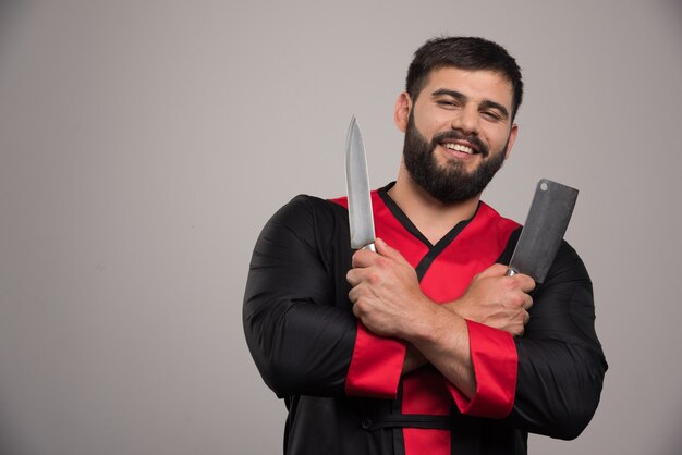 Free Photo | Smiling man holding two knifes on grey wall