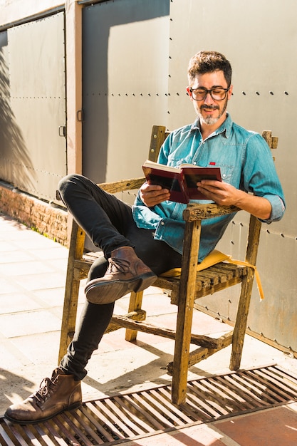 Smiling man sitting on wooden chair reading the book