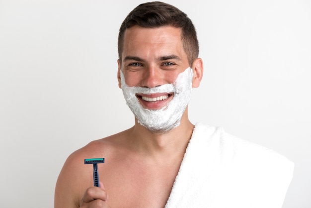 Smiling man with towel applied shaving cream holding razor looking at camera Free Photo