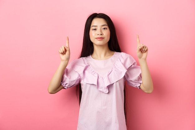 Premium Photo | Smiling teen girl asian pointing fingers up at empty ...