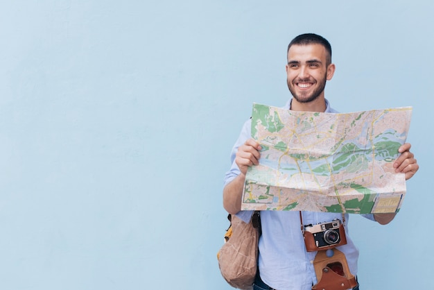 Smiling traveler photographer holding map and looking away standing against blue backdrop Free Photo