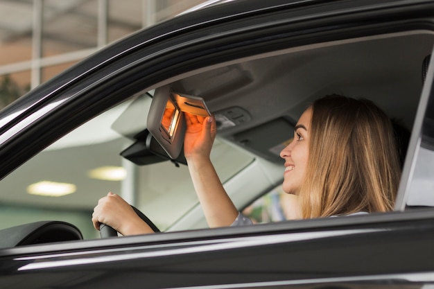 車の鏡で見ている笑顔の女性 無料の写真