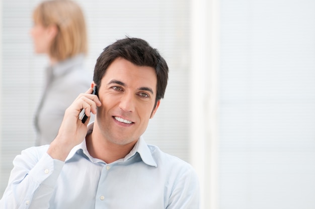 Premium Photo | Smiling young businessman talking on mobile at work in ...