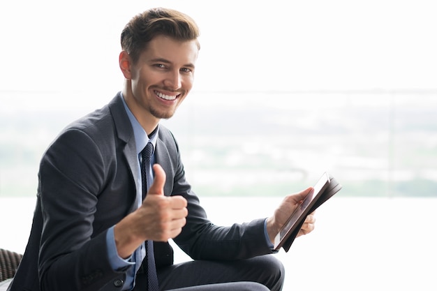 Smiling young businessman with thumb up and tablet Free Photo