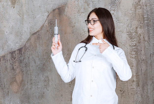 Free Photo Smiling Young Female Doctor Holding Injection And Pointing