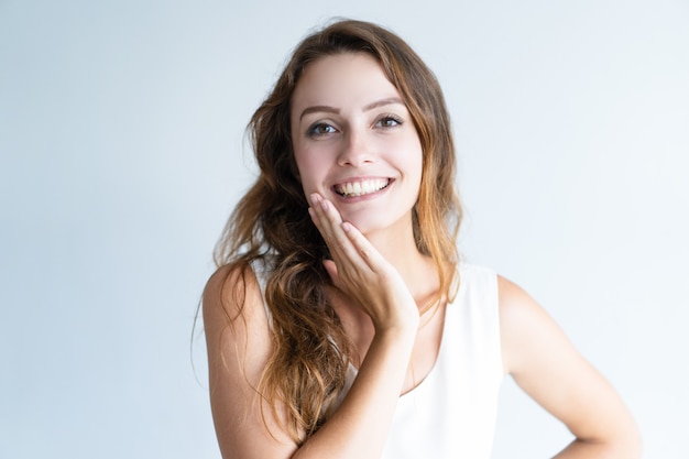 Smiling young lovely woman looking at camera and touching face Free Photo