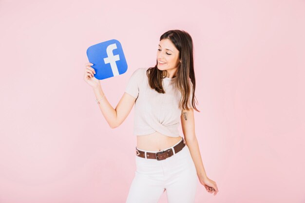 Smiling young woman holding facebook icon on pink background | Free Photo