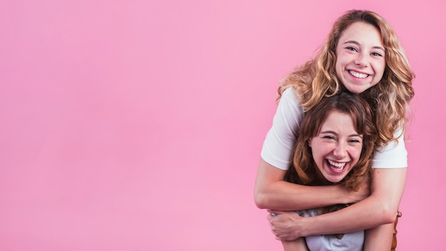 Smiling Young Woman Hugging Her Friend From Behind Against Pink