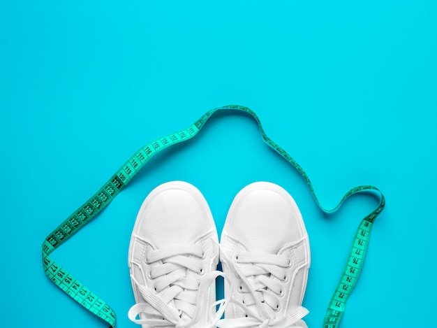 Sneakers are tied with measuring on a blue background. the concept of an active lifestyle, the layout of the apartment. promotion of walking and a bonus weight loss. top view. Premium Photo