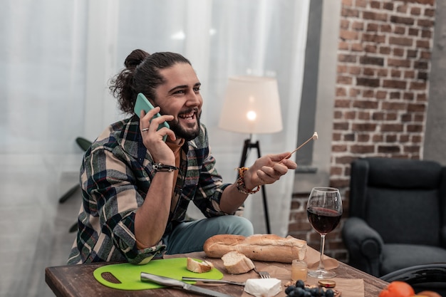 So tasty. cheerful positive man eating delicious cheese while talking on the phone Premium Photo