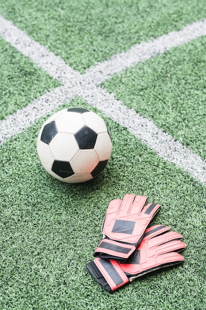 交差した白い線との試合のための緑のフィールド上のサッカー選手のサッカーボールと革手袋 プレミアム写真