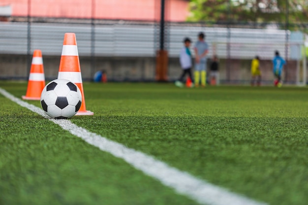 サッカーボールの戦術は 背景を訓練するための芝生のフィールドにコーンサッカーで子供たちを訓練する プレミアム写真