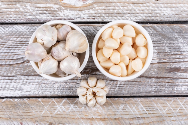 Some garlic in a bowls and nearby on wooden table, top view. Free Photo