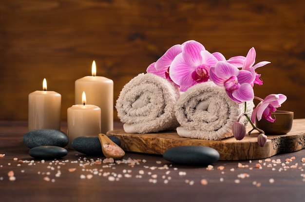  Spa setting with brown rolled towel and orchids and candles on wood. Premium Photo