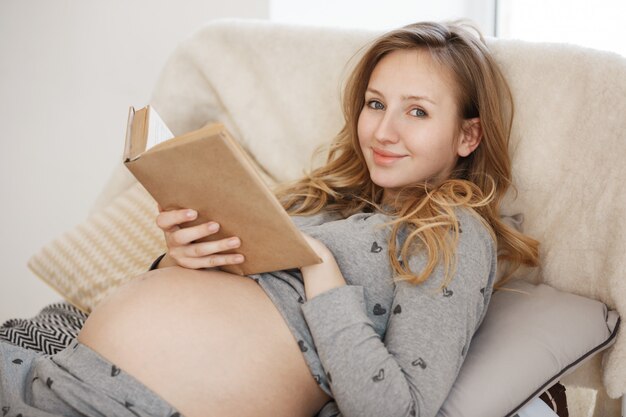 Free Photo Spending Precious Time Of Soon Ending Pregnancy Portrait Of Young Charming Cheerful Pregnant Mother With Blond Hair Lying In Bed Reading Favorite Book Relaxing In Morning