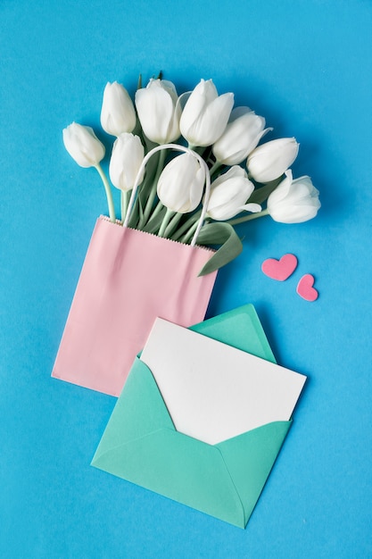 Download Springtime flat lay, white tulips in paper bag on blue mint background with envelope, blank card ...