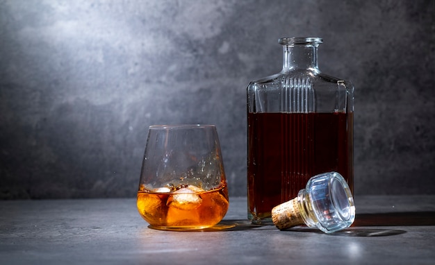 Premium Photo | Square whiskey bottle and glass with ice on dark gray