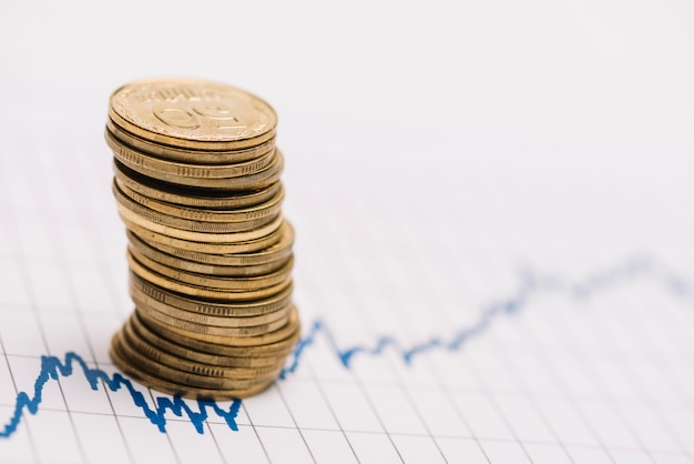 Stack of golden coins over the stock market graph on single line paper Free Photo