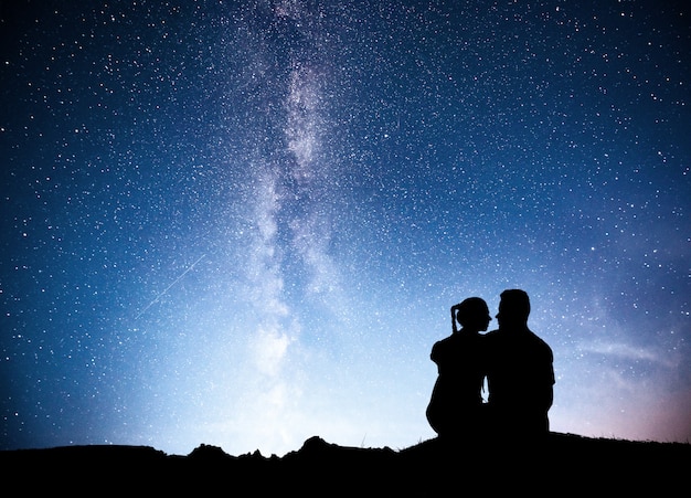 Uomo e donna in piedi sulla montagna con la luce delle stelle. abbracciare  le coppie contro la via lattea viola. | Foto Gratis