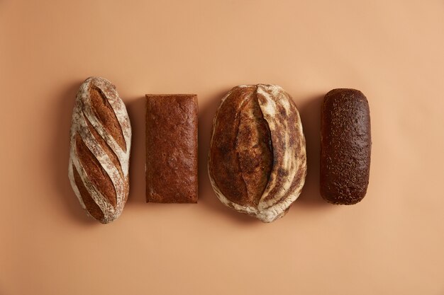 Staple food and healthy nutrition concept. four types of bread isolated on brown background. wheat, rye, spelt bread enriched with vitamins and minerals, made of organic flour, has health benefits Free Photo