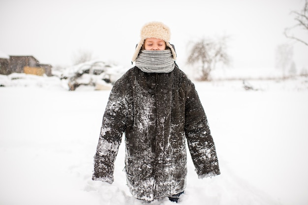 ロシアの村の冬の日に雪道に立っている着用した特大の服を着た奇妙な少女 プレミアム写真