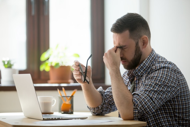 Stressed male massaging nose bridge suffering from headache Free Photo