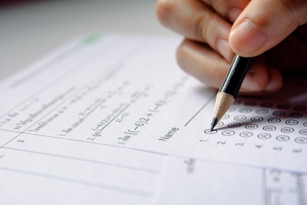 Students hand holding pencil writing selected choice on answer sheets and mathematics question sheets Premium Photo