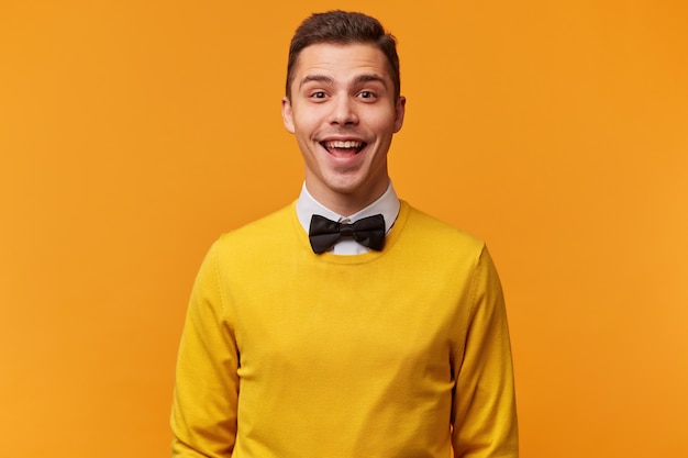 蝶ネクタイ付きの黄色いセーターを着た 楽しく社交的な若い魅力的な男のスタジオショット 無料の写真