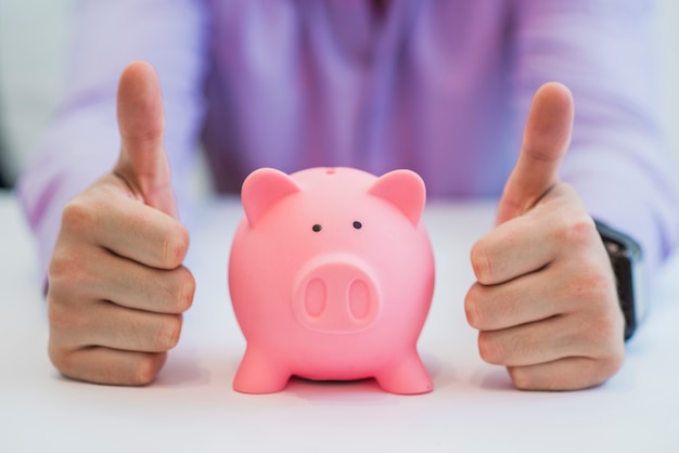 Successful business man with piggy bank holding thumbs up in office Free Photo